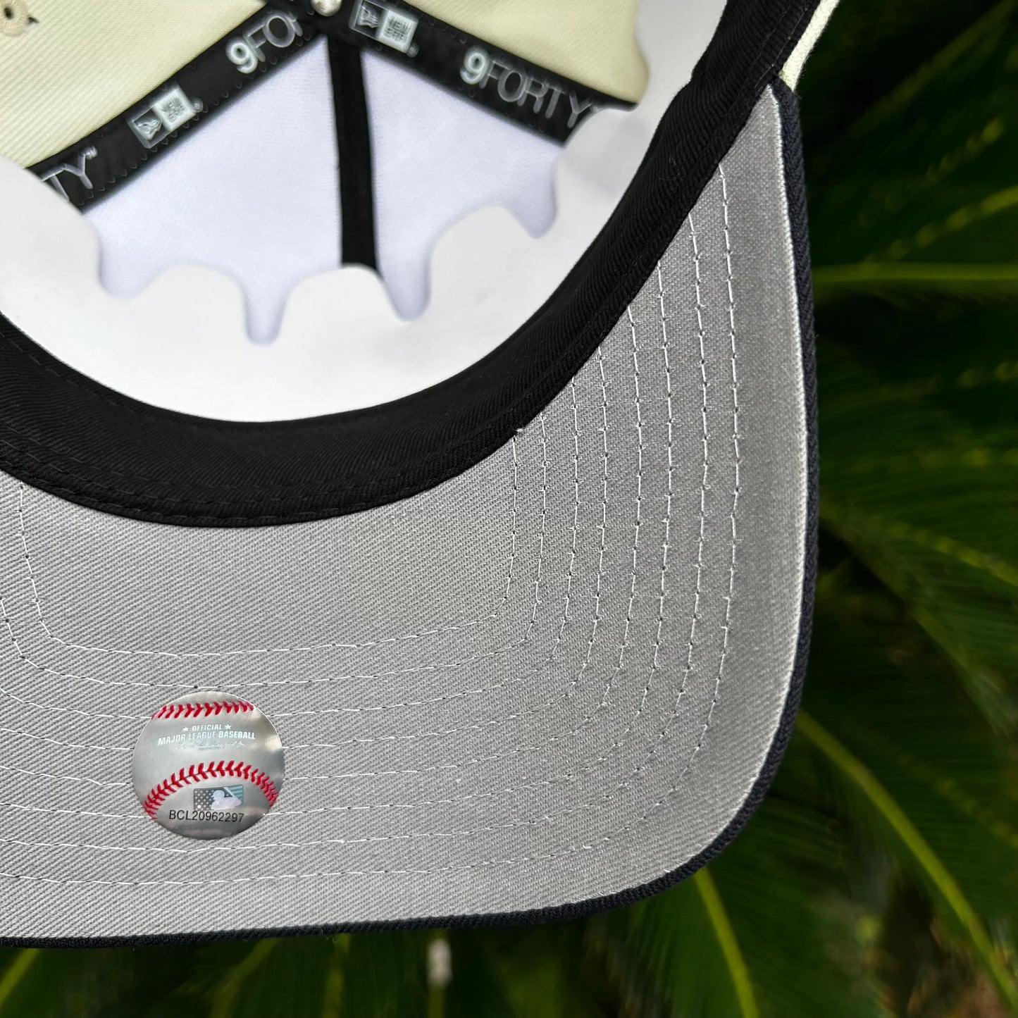 Detalle interior de gorra New Era 9FORTY con etiqueta oficial de MLB sobre fondo de hojas verdes