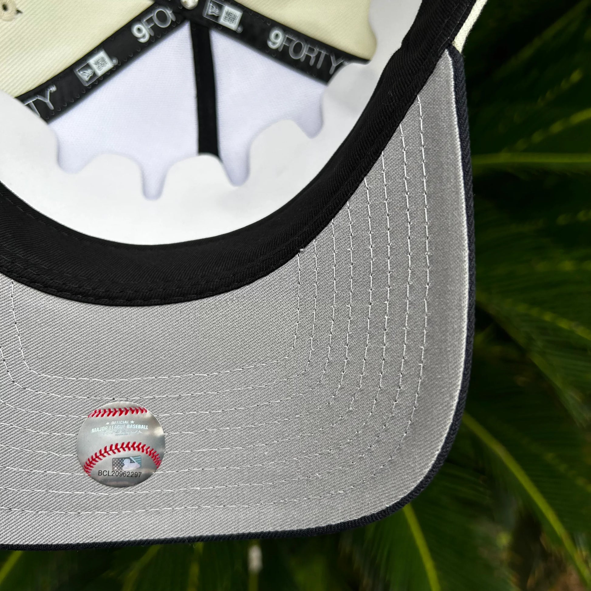 Detalle interior de gorra New Era 9FORTY con etiqueta oficial de MLB sobre fondo de hojas verdes