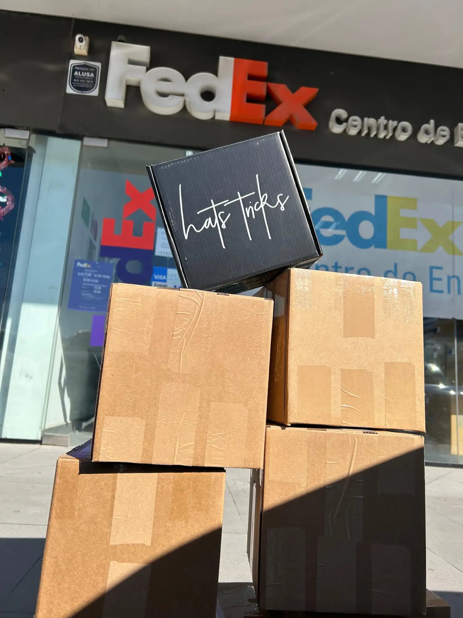 Caja rectangular negra con texto en cursiva blanco 'hats tricks' en la tapa.