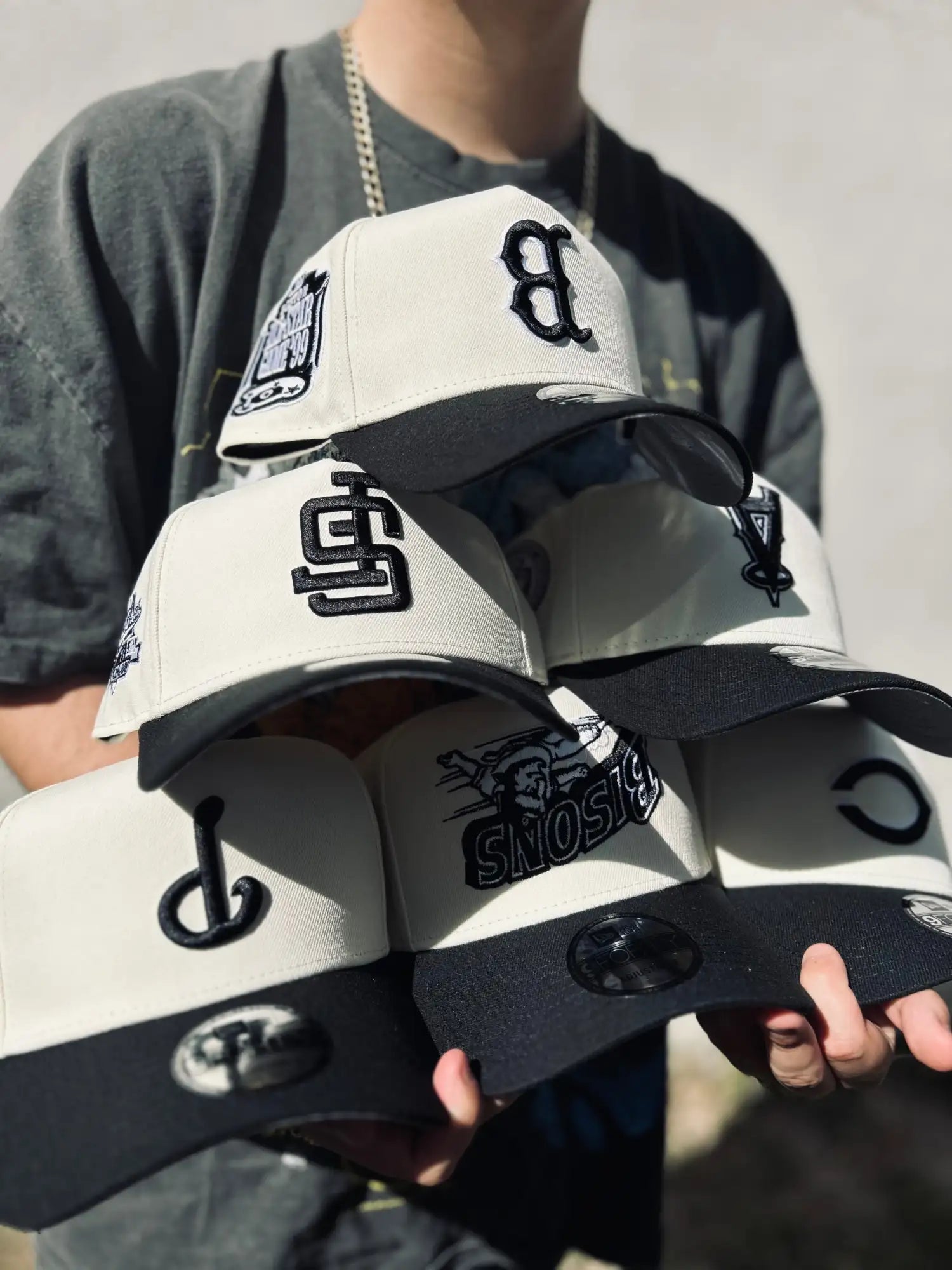 Una pila de gorras de béisbol new era en crema y negro con logos bordados.